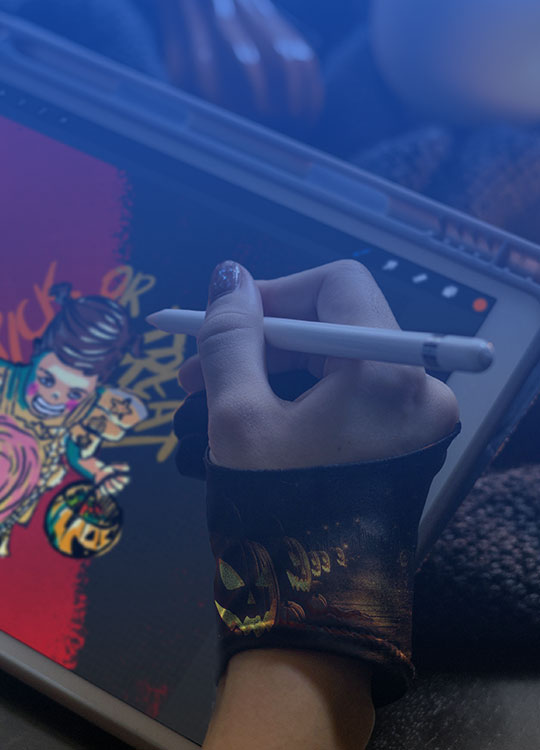 Digital artist drawing a Halloween-themed illustration on a tablet using a stylus, wearing artse gloves with pumpkin designs